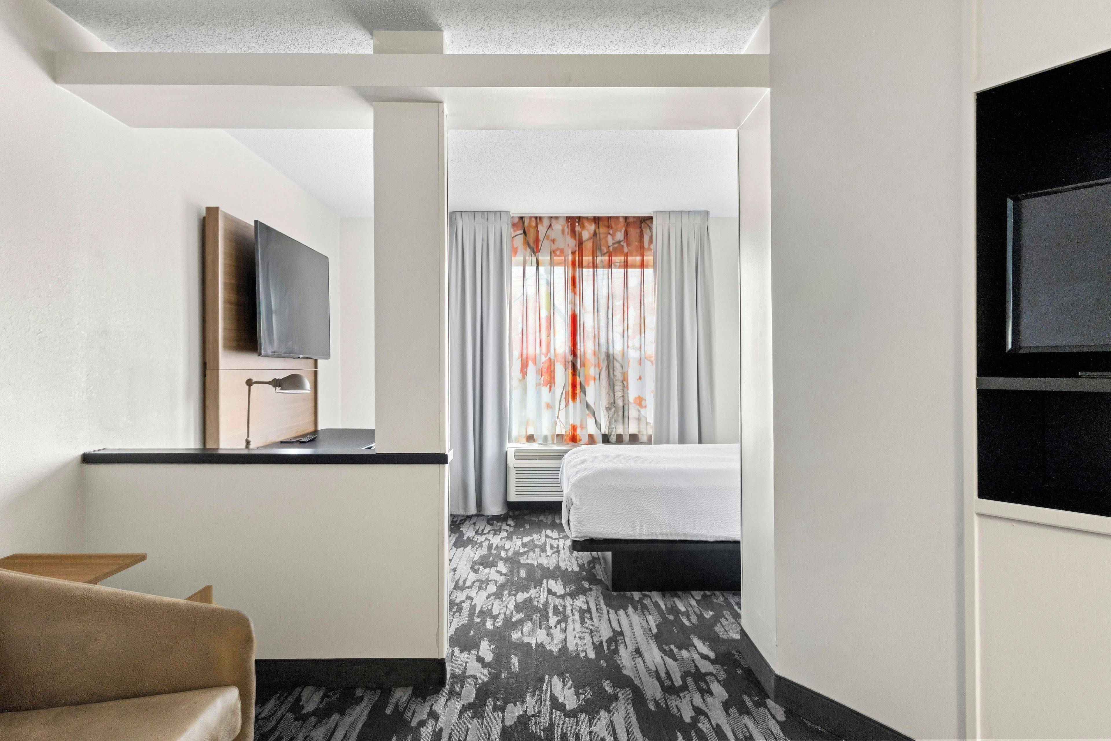 Une chambre d’hôtel comprenant un lit, un bureau avec un téléviseur à  écran plat, une chaise et une fenêtre avec des rideaux.