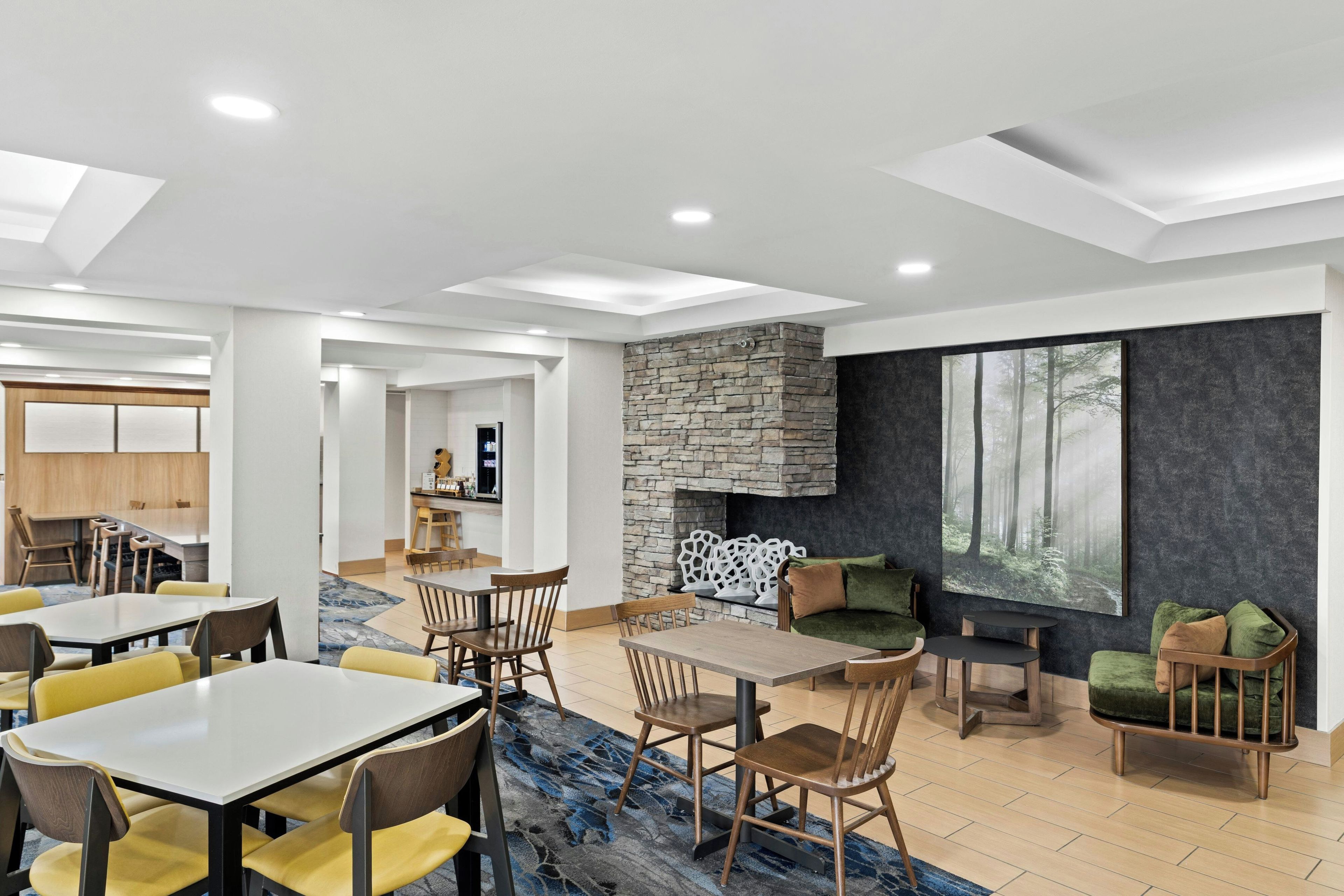 A modern interior with a stone fireplace, dining area, and seating with a view of a forest through large windows.