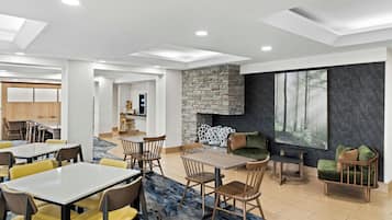 A modern interior with a stone fireplace, dining area, and seating with a view of a forest through large windows.