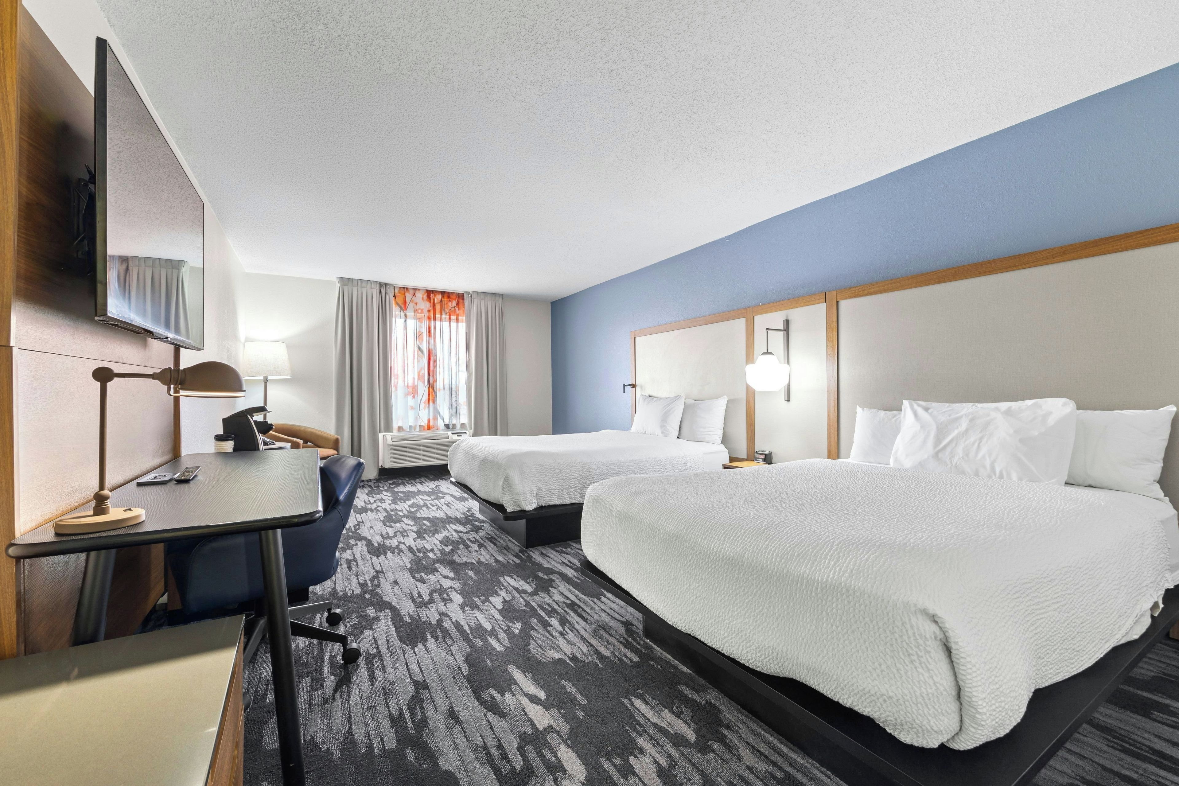 A hotel room with two beds, a desk, a chair, a TV, and a window with curtains.