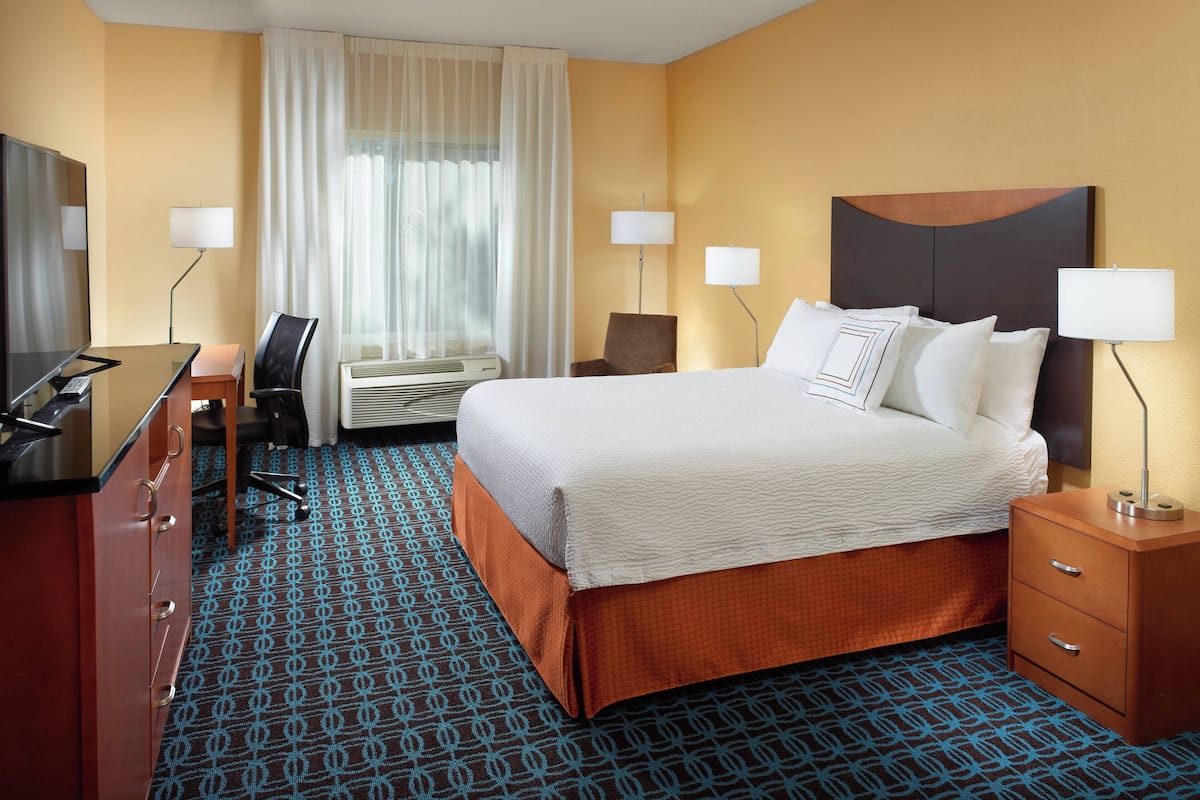 Una habitación de hotel con cama, mesitas de noche, un escritorio con silla, aire acondicionado y televisión.