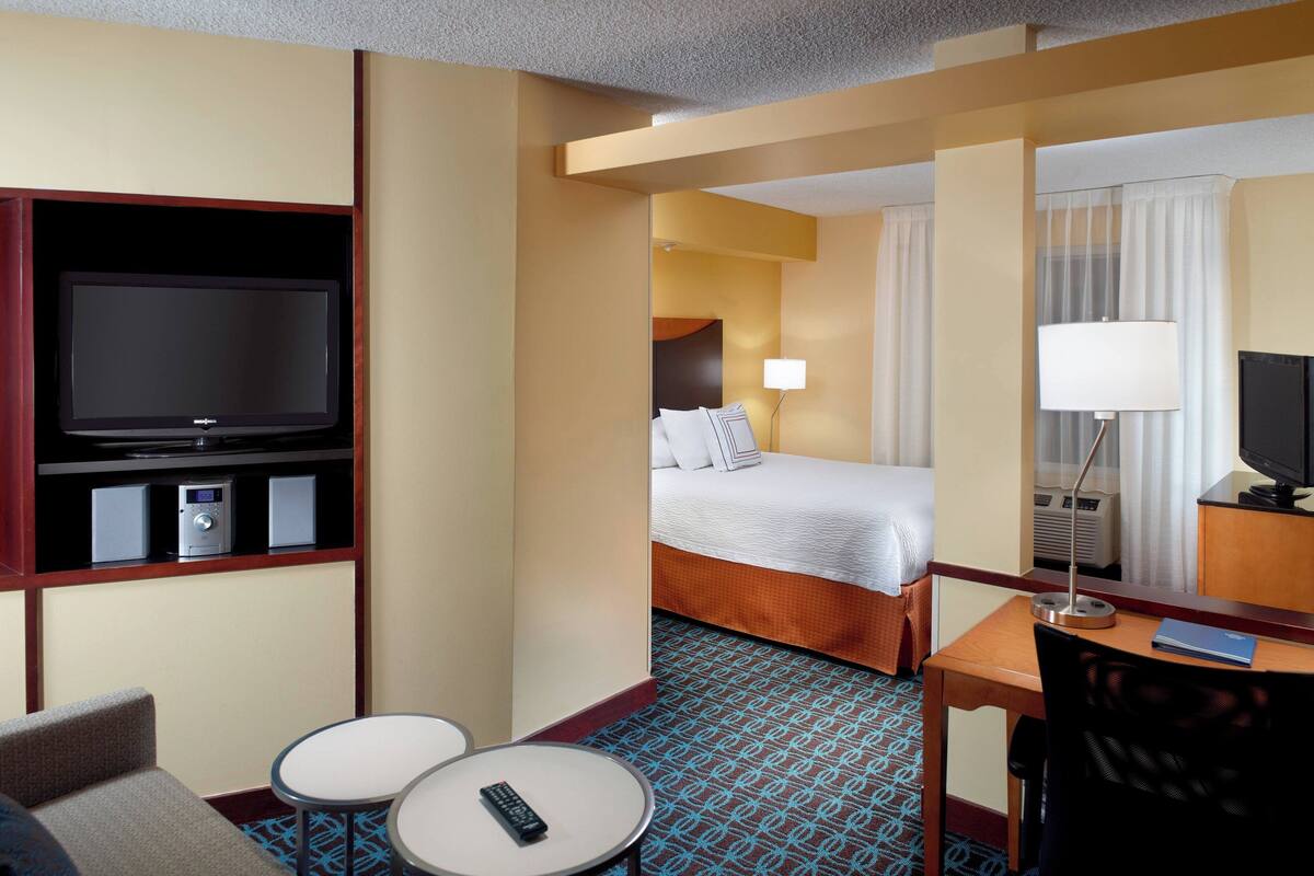 Una habitación de hotel con cama, escritorio, silla, televisor y una mesita.