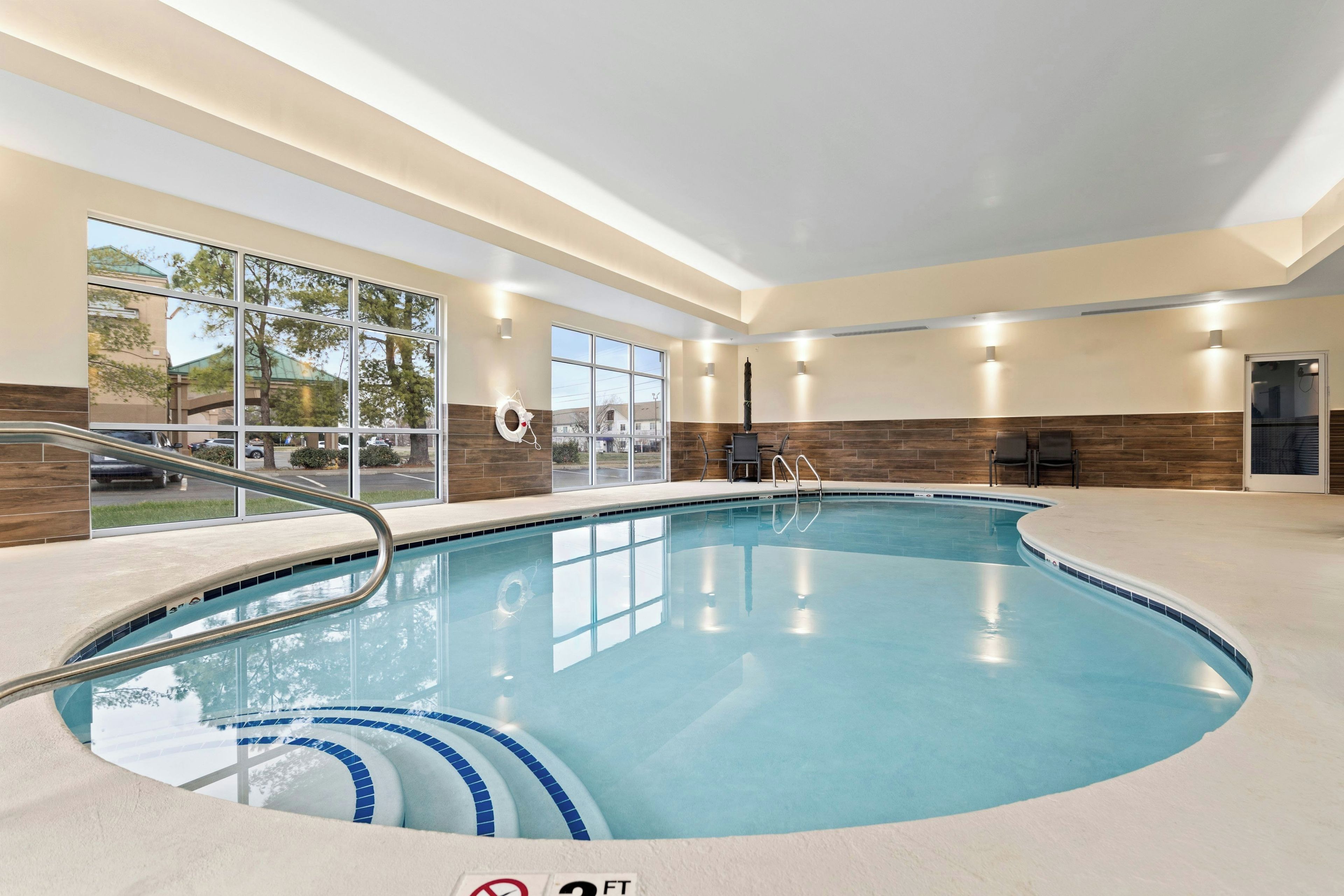 An indoor swimming pool with clear water, a lifeguard chair, and a view of the outside through large windows.