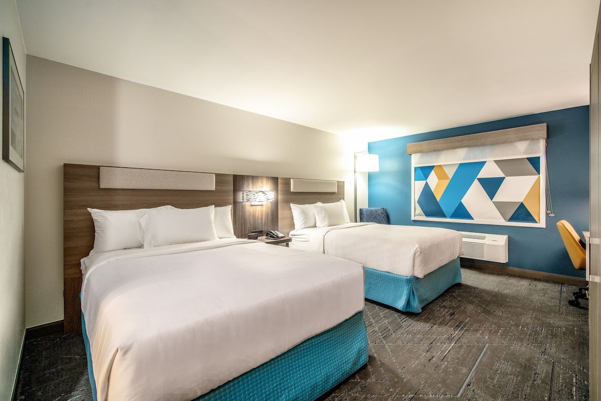 Habitación de hotel con dos camas, cabecero de madera, teléfono en la pared y decoración mural con diseño geométrico.