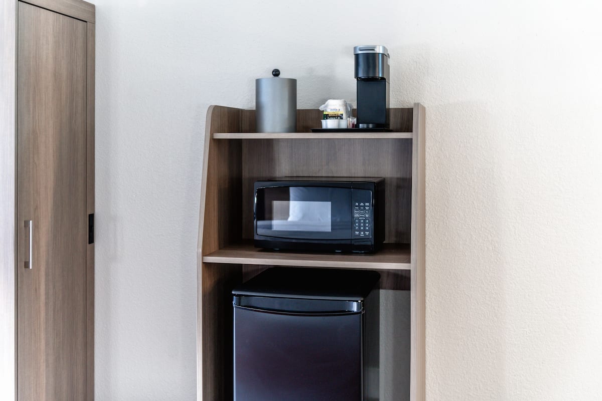 Una kitchenette compacta con microondas, cafetera y un refrigerador pequeño.