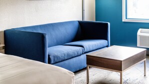Ein Zimmer mit einem blauen Sofa, einem Holztisch und einem weißen Bett.