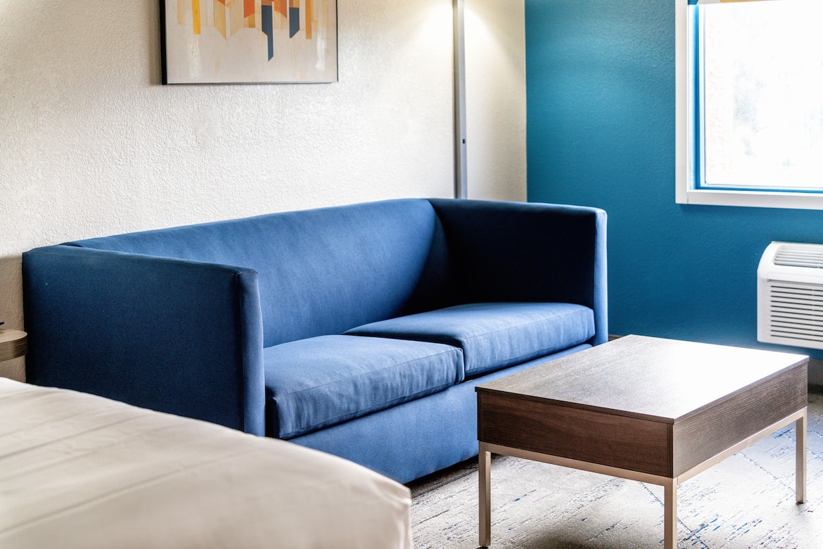 Una habitación con un sofá azul, una mesa de centro de madera y una cama blanca.