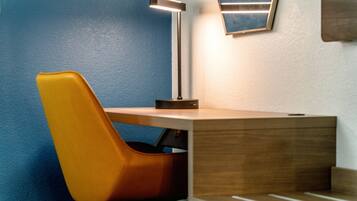 Un rincón de una habitación con un escritorio de madera, una lámpara moderna y una pared azul.