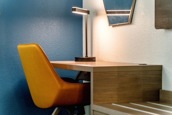 A corner of a room with a wooden desk, a modern lamp, and a blue wall.