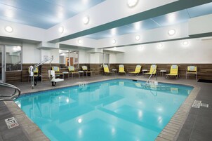 A swimming pool with clear blue water, yellow lounge chairs, and a tiled deck.