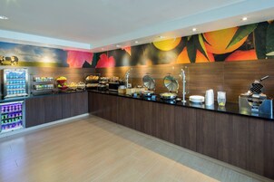 A buffet area with a variety of food options, a beverage dispenser, and a fruit bowl.