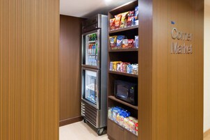 A corner with a vending machine stocked with snacks and beverages, a microwave, and a shelf with packaged goods.