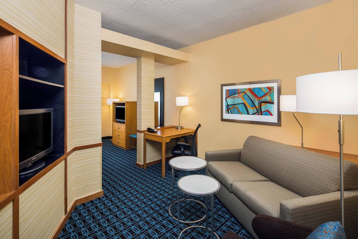 A hotel room with a sofa, a TV, a desk with a chair, a lamp, and a painting on the wall.