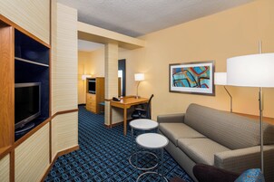 A hotel room with a sofa, a TV, a desk with a chair, a lamp, and a painting on the wall.