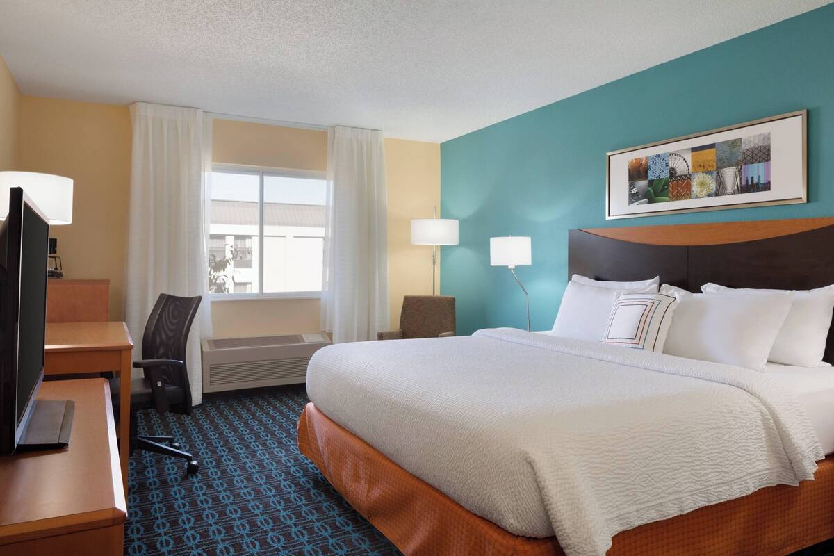 Een hotelkamer met een bed, een bureau, een stoel, een televisie en een raam met gordijnen.