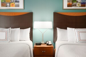 Quarto de hotel com duas camas, uma mesa de cabeceira com uma luminária, um relógio e um telefone.