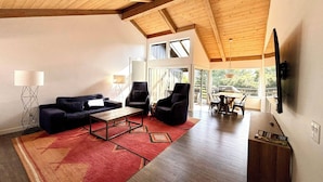 A spacious living area with a high ceiling, wooden beams, a large window, and a dining area with a table and chairs. - Hidden Valley Inn (Carmel Valley)