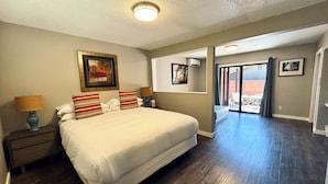 A hotel room with a large bed, two bedside tables with lamps, a ceiling light, a large mirror, and a sliding glass door leading to a balcony. - Hidden Valley Inn (Carmel Valley)