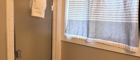 Un baño con puerta de vidrio para la ducha, una toalla colgada en la puerta, una cortina de baño a rayas y un dispensador de papel higiénico.