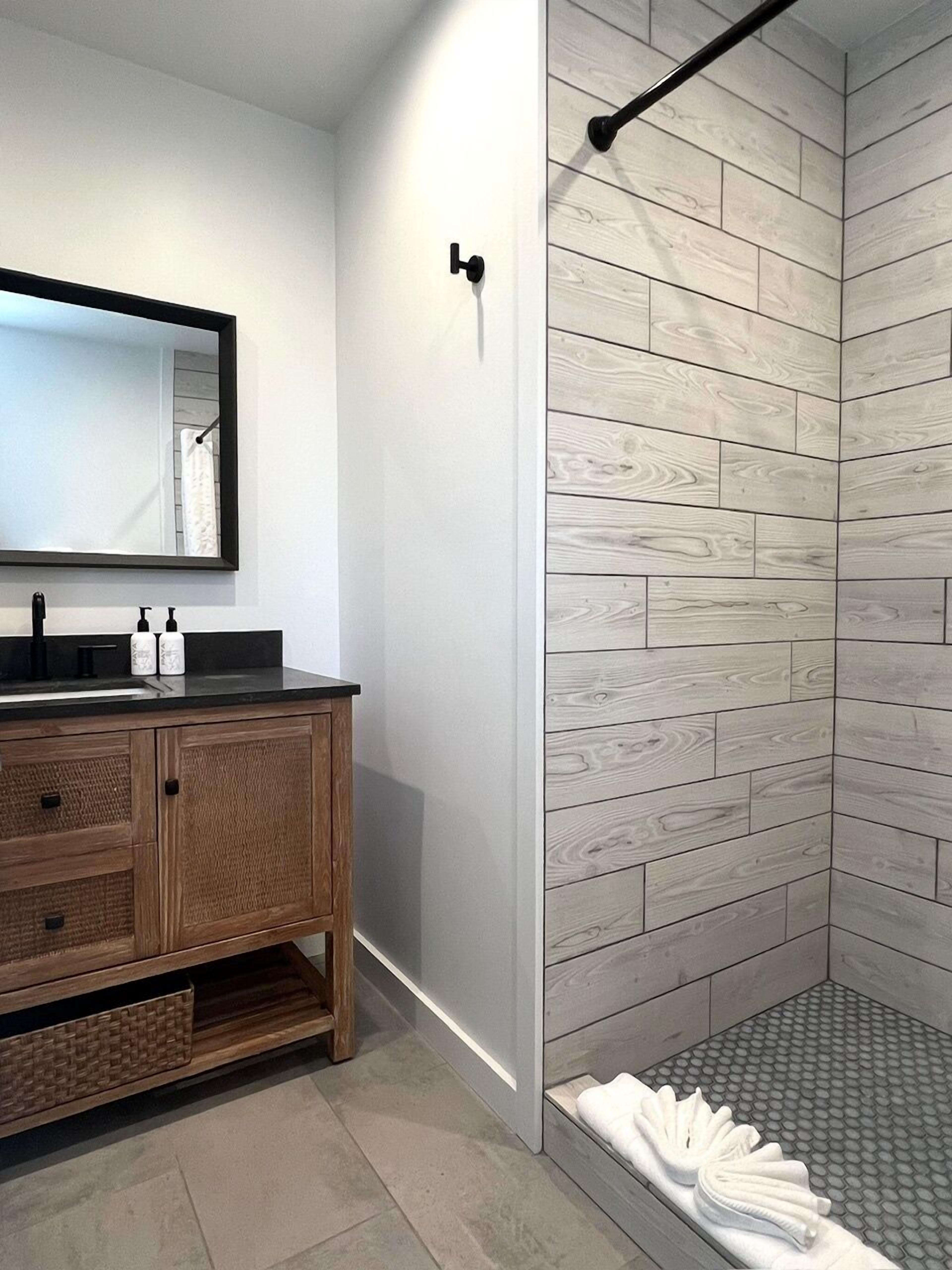 A modern bathroom with a wooden vanity, a large mirror, and a shower area with a textured wall.