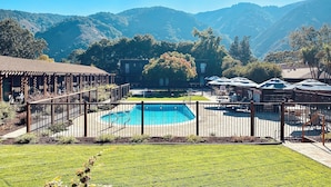 A pool area with a fenced deck, lounge chairs, and a view of mountains. - Hidden Valley Inn (Carmel Valley)