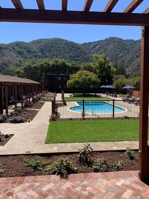 A pool area with a wooden pergola, a brick pathway, and a view of a mountain range.