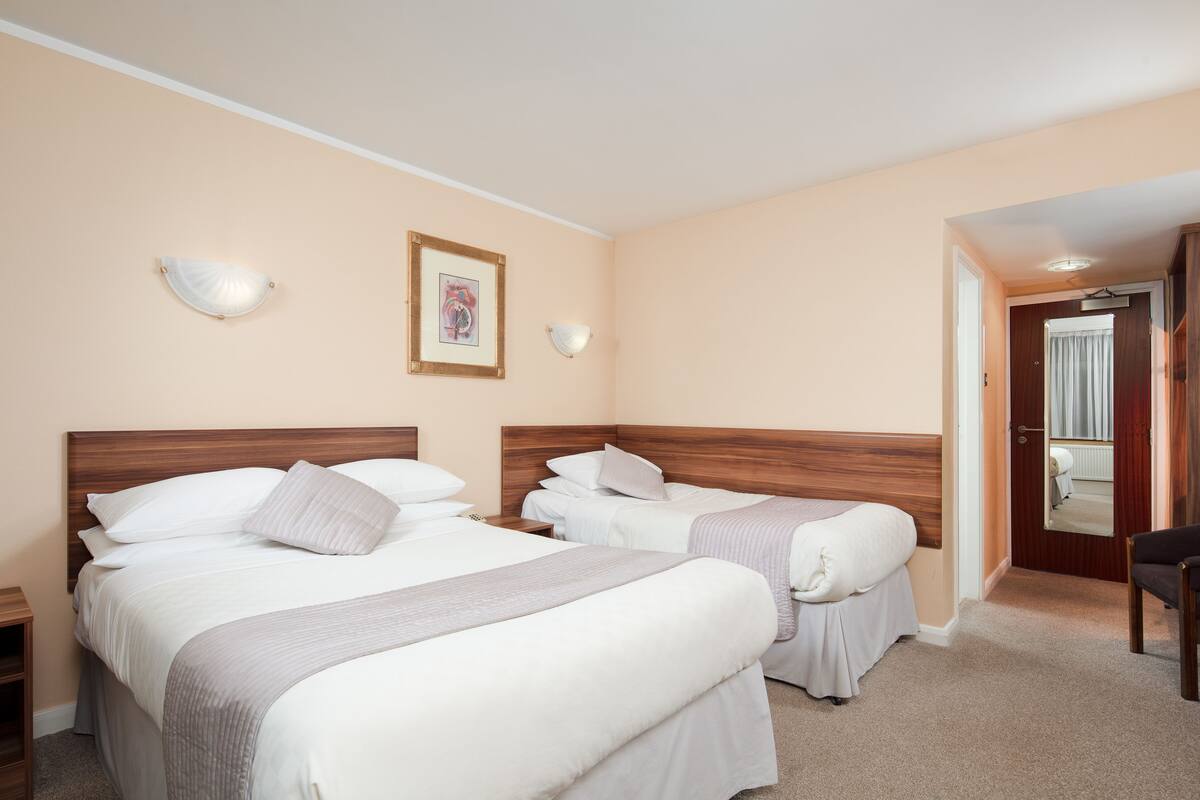 A hotel room with two beds, a wooden headboard, a framed picture, and a mirror on the wall.