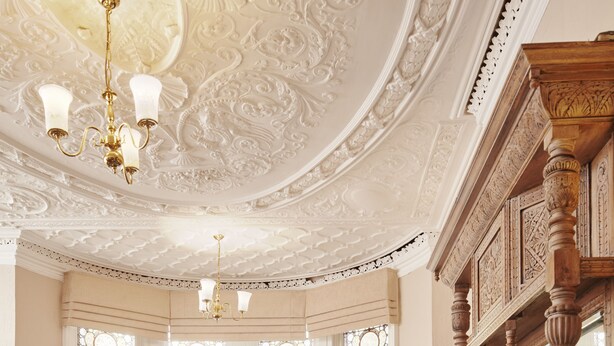 Une pièce dotée d’un plafond richement décoré, d’une cheminée et d’une grande fenêtre ornée de vitraux.