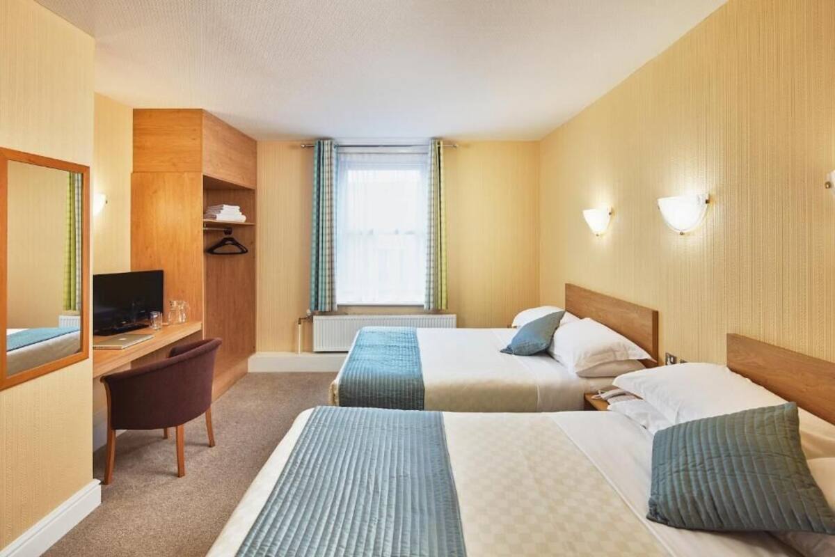 A hotel room with two beds, a desk with a chair, a television, and a window with curtains.