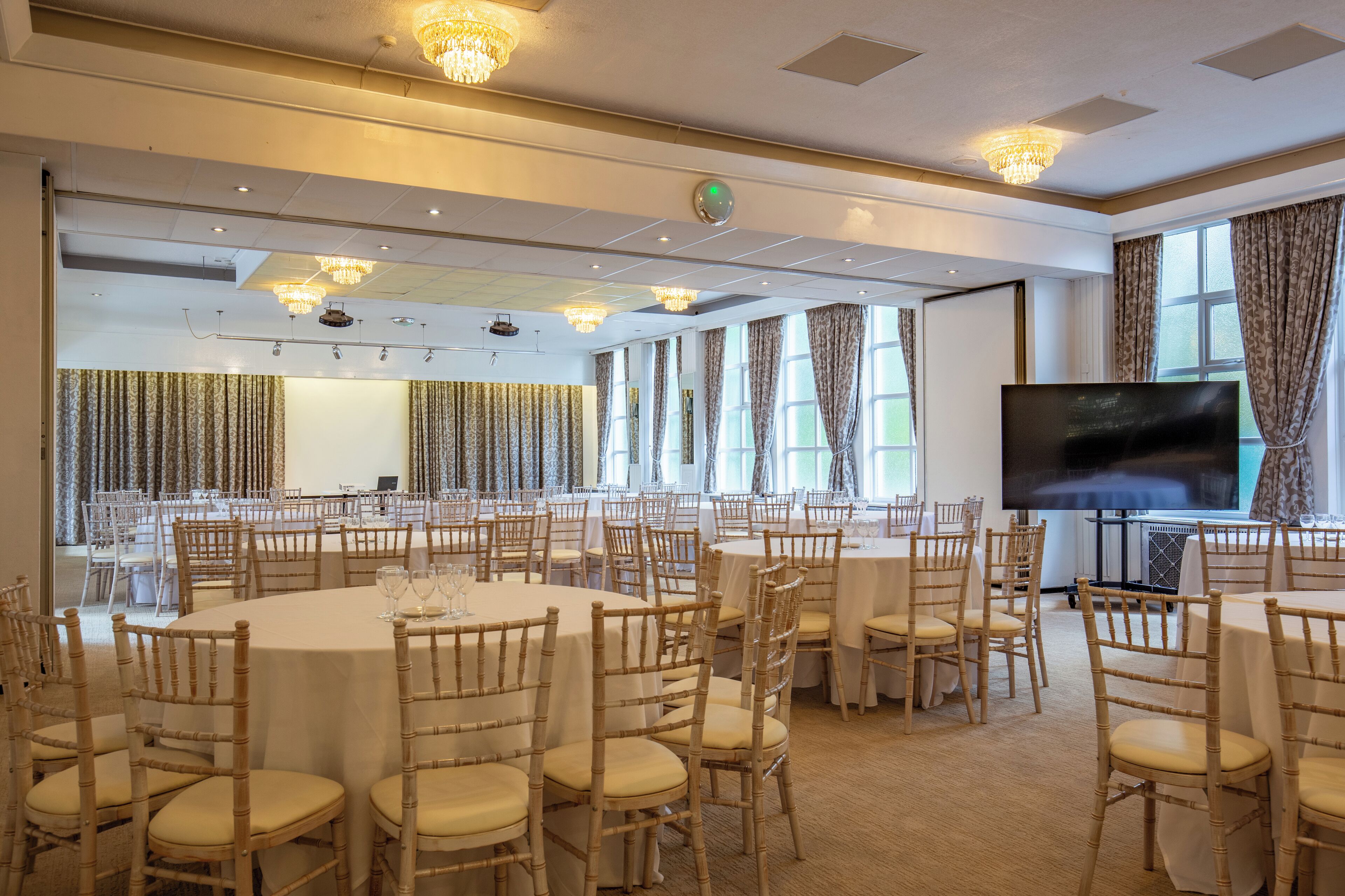 Un salón de conferencias amplio con mesas y sillas redondas, una pantalla grande y candelabros.