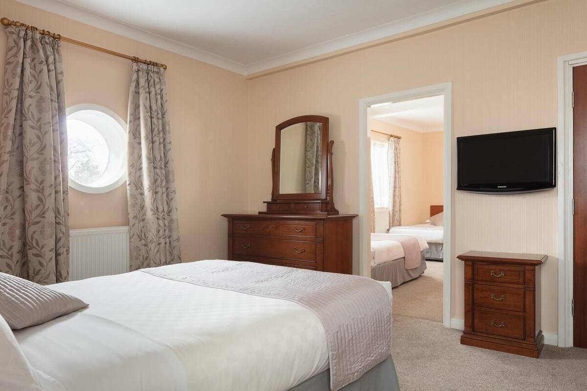 A bedroom with a bed, dresser, mirror, television, and a window with curtains.