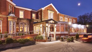 Un hôtel à l’architecture traditionnelle, avec une façade en briques, une entrée imposante surmontée d’un auvent et un espace restaurant bien visible.