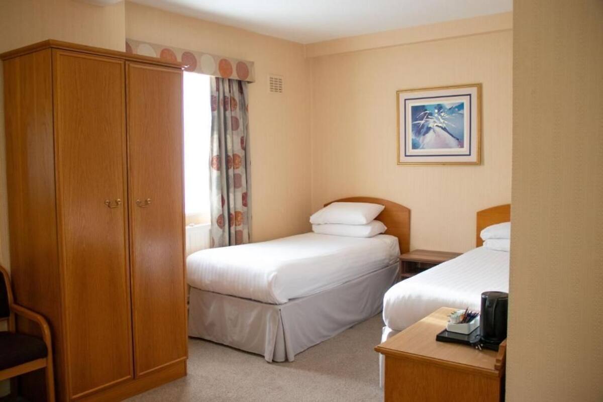 A hotel room with two beds, a wardrobe, a desk with a coffee maker, and a framed picture on the wall.