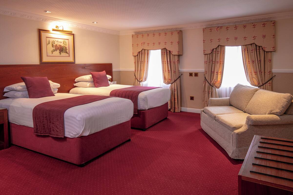 Habitación de hotel con dos camas, un sofá y una mesita de madera.