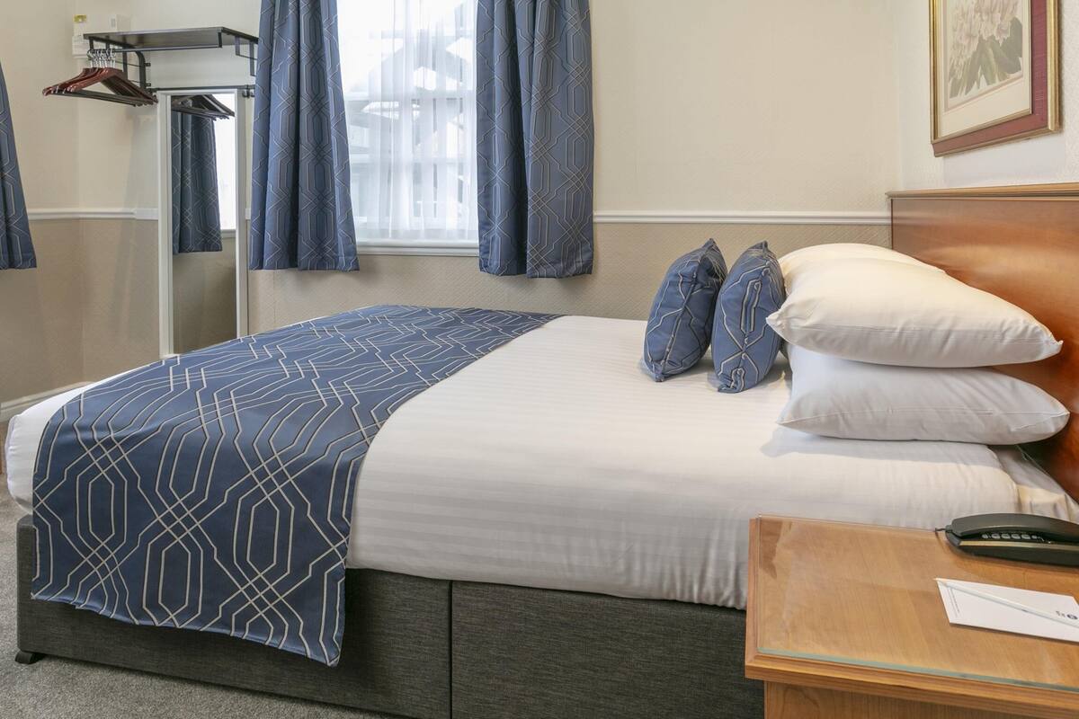 Una habitación de hotel con cama, una silla, una mesita de noche y una ventana con cortinas.