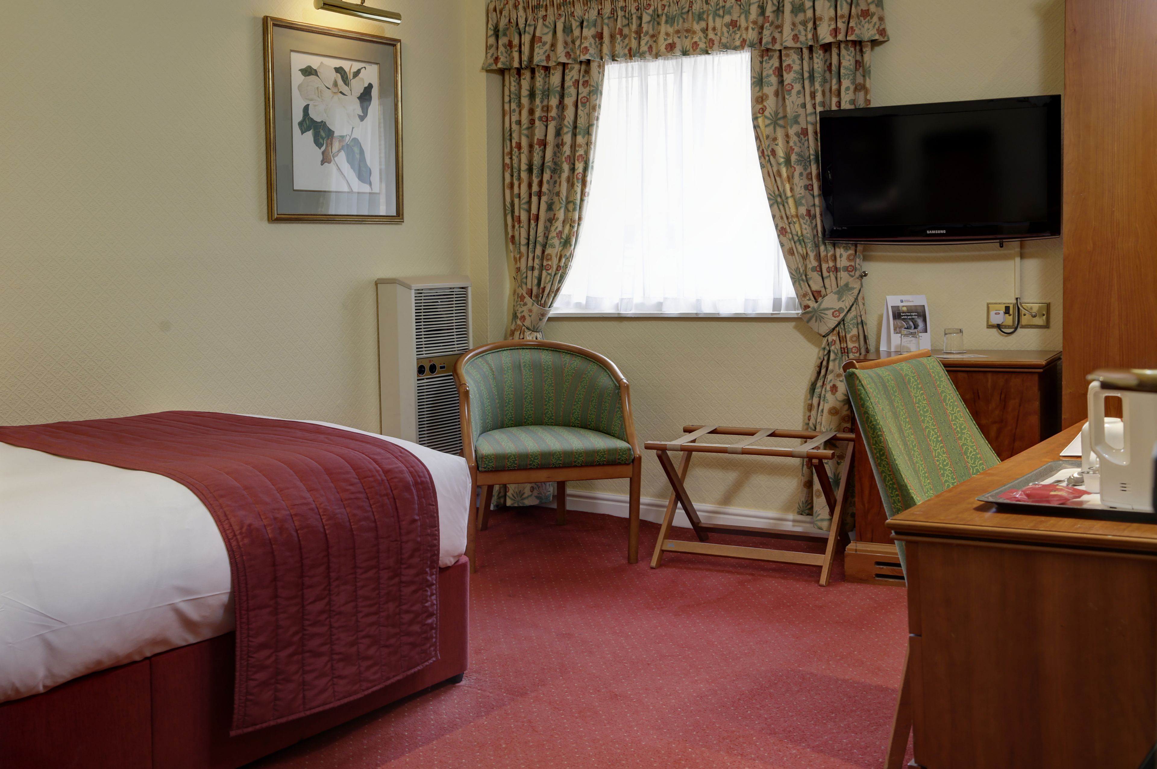 A hotel room with a bed, a chair, a desk, a television, and a window with curtains.