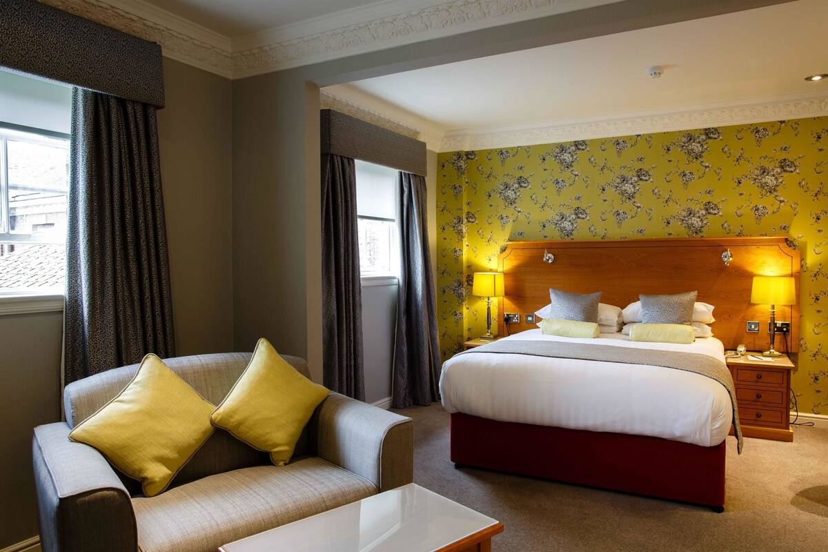 Una habitación de hotel con cama, sofá, mesita de noche y lámpara.