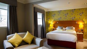 A hotel room with a bed, a sofa, a nightstand, and a lamp.