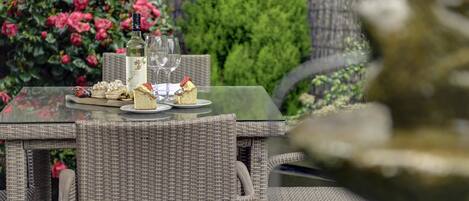 A wicker table set with a bottle of white wine, glasses, and various desserts.