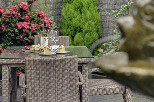 A wicker table set with a bottle of white wine, glasses, and various desserts.