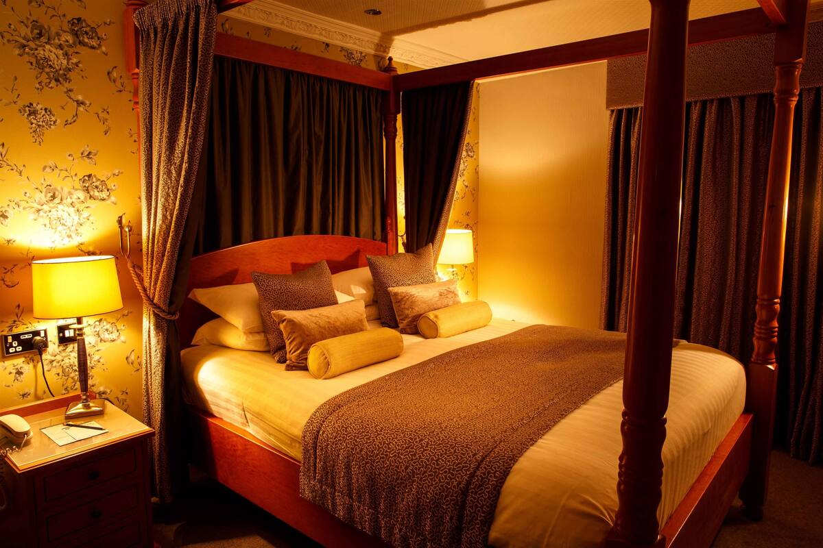 Una cama con dosel y cortinas, una mesita de noche con lámpara y un teléfono.
