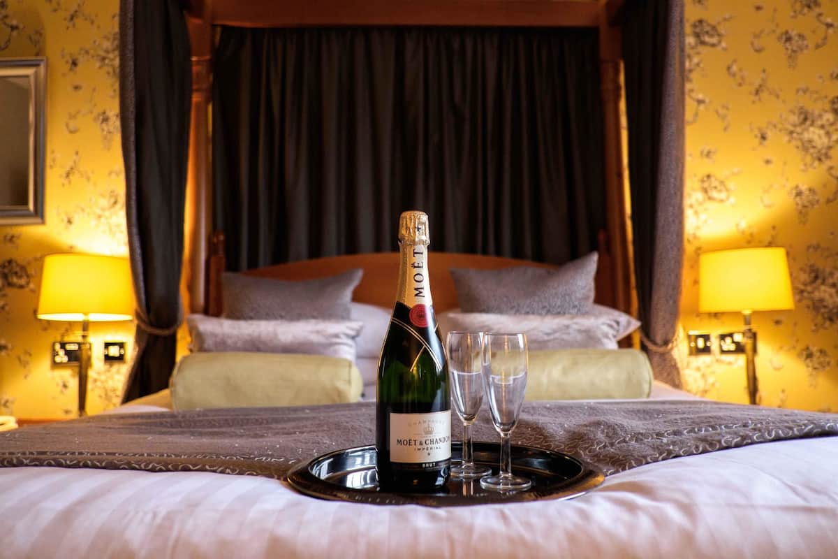 Una botella de champán Moët & Chandon sobre una bandeja con dos copas en una cama dentro de una habitación con dosel y cortinas.