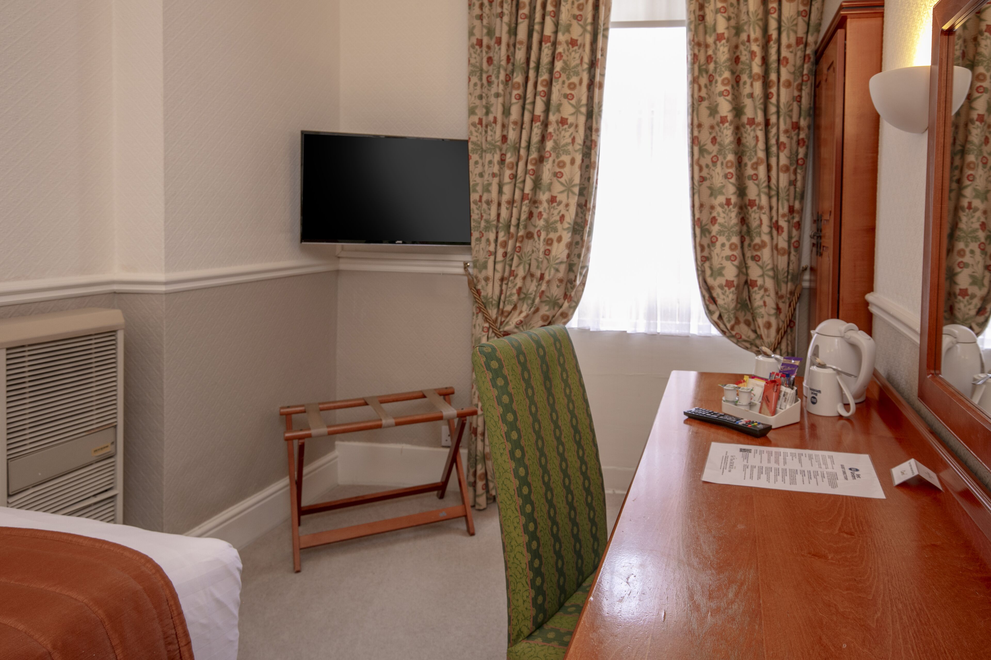 A hotel room with a bed, a chair, a desk with a coffee maker, a television, and a window with curtains.