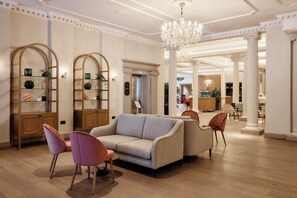 Un hall d’entrée spacieux, agrémenté d’un magnifique lustre, de colonnes en bois et d’un espace détente avec des canapés et des fauteuils.