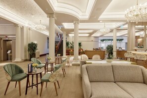 Un vestíbulo espacioso con una imponente escalera, candelabros elegantes y un mostrador de recepción.