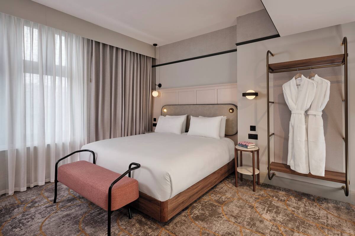 Une chambre d’hôtel avec un grand lit, un banc, un porte-peignoir et une petite table.