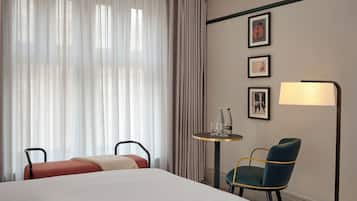 A hotel room with a large bed, two chairs, a small table with bottles and glasses, a lamp, and framed pictures on the wall.