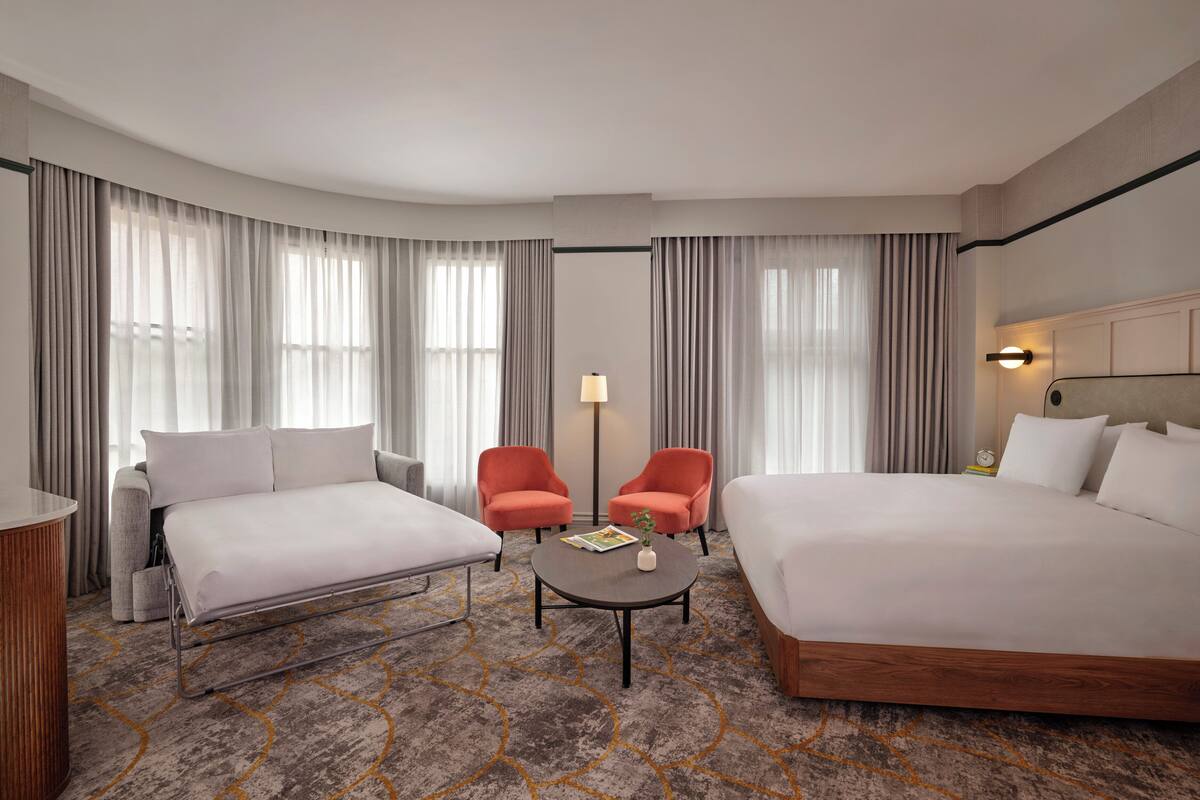 Une chambre d’hôtel avec un grand lit, deux fauteuils, une petite table et un canapé.