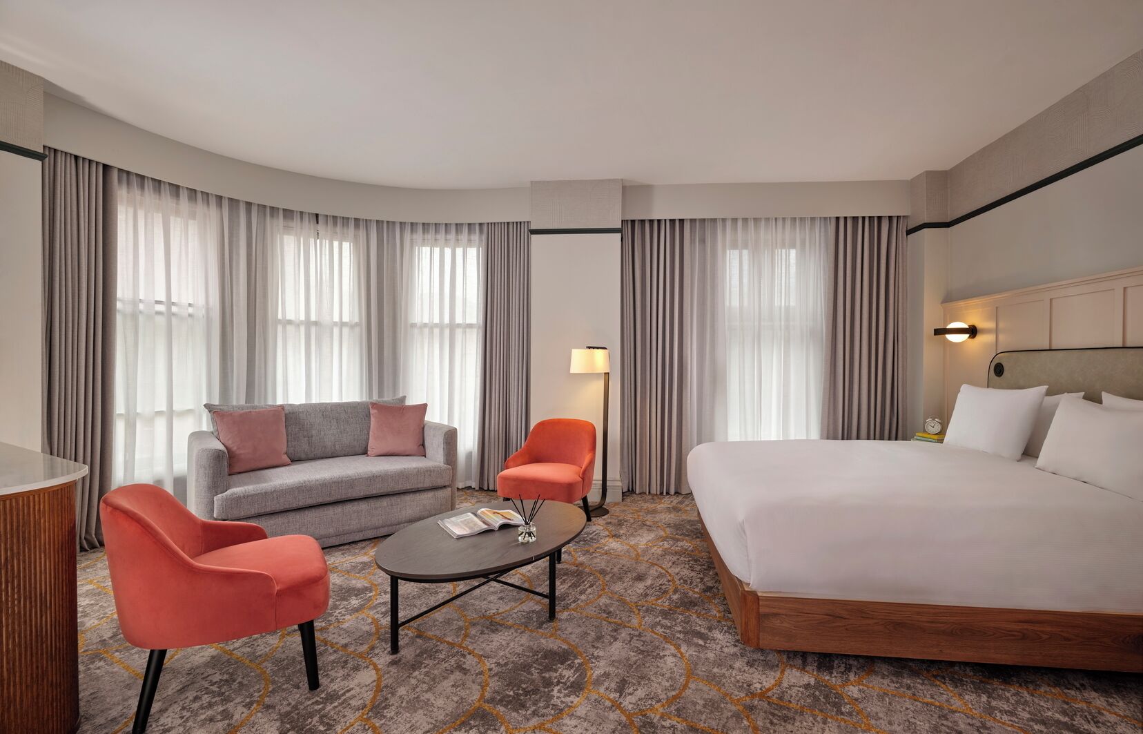 A hotel room with a bed, a sofa, two armchairs, a coffee table, and a lamp.