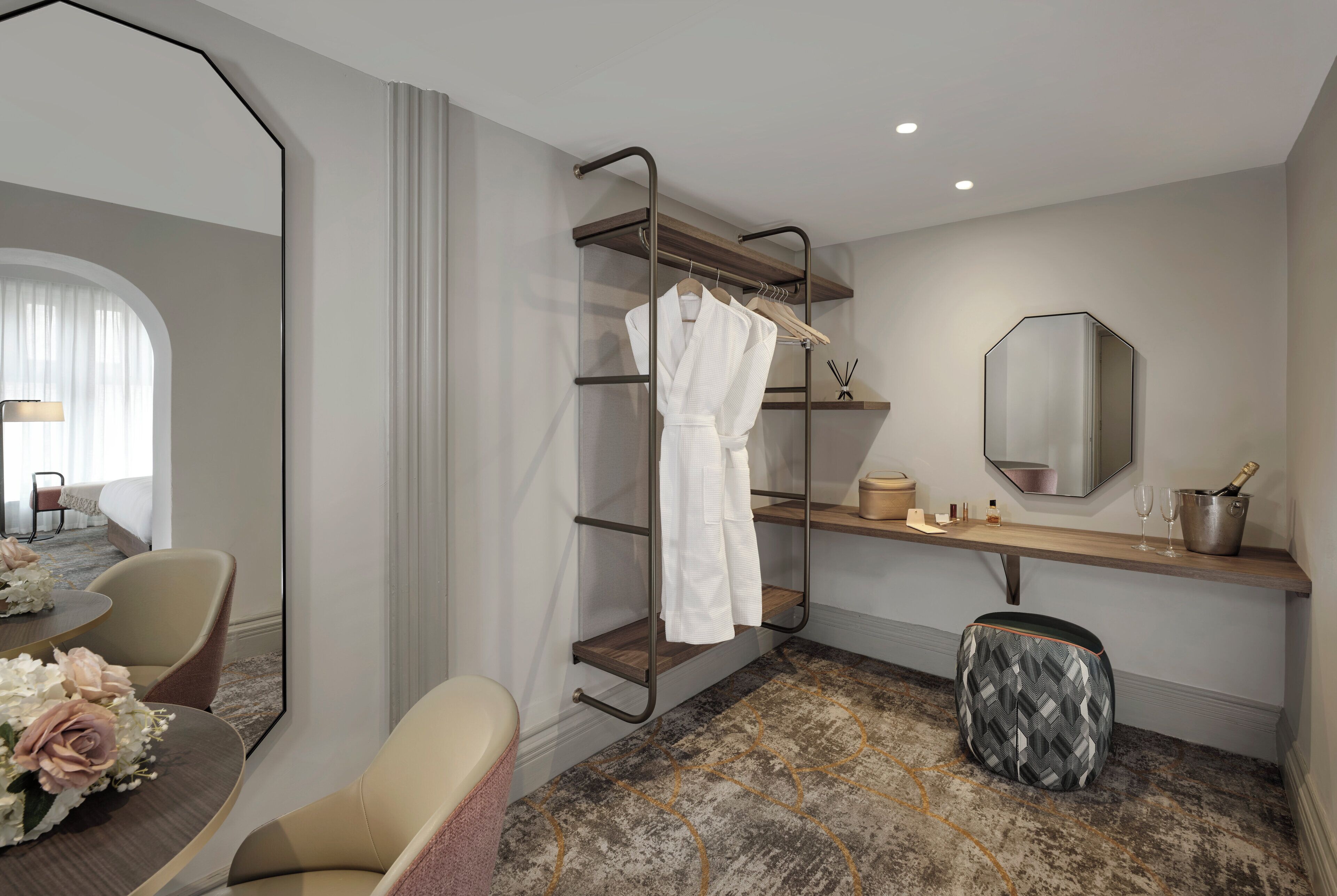 Une chambre d’hôtel comprenant un coin salon, une coiffeuse avec un miroir, un porte-peignoir et une petite table avec des articles de toilette.